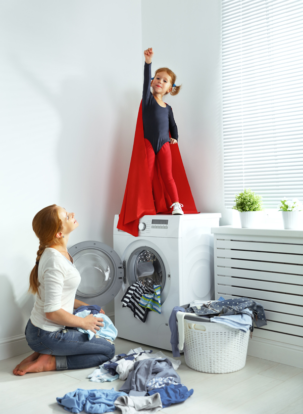 Une mère et sa petite fille habillée en super-héros dans une buanderie près de la machine à laver et des vêtements sales