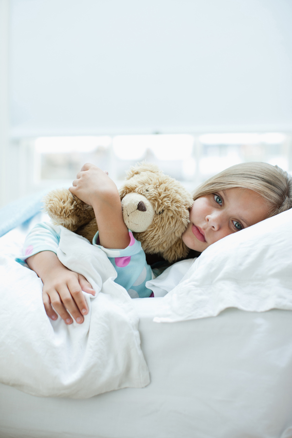 Une petite fille malade dans son lit avec un nounours